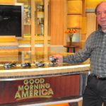 A man standing in front of a bar with coffee cups on it.