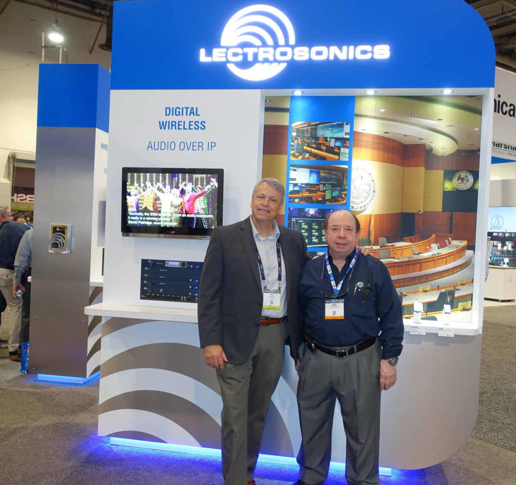 Two men standing in front of a large sign.